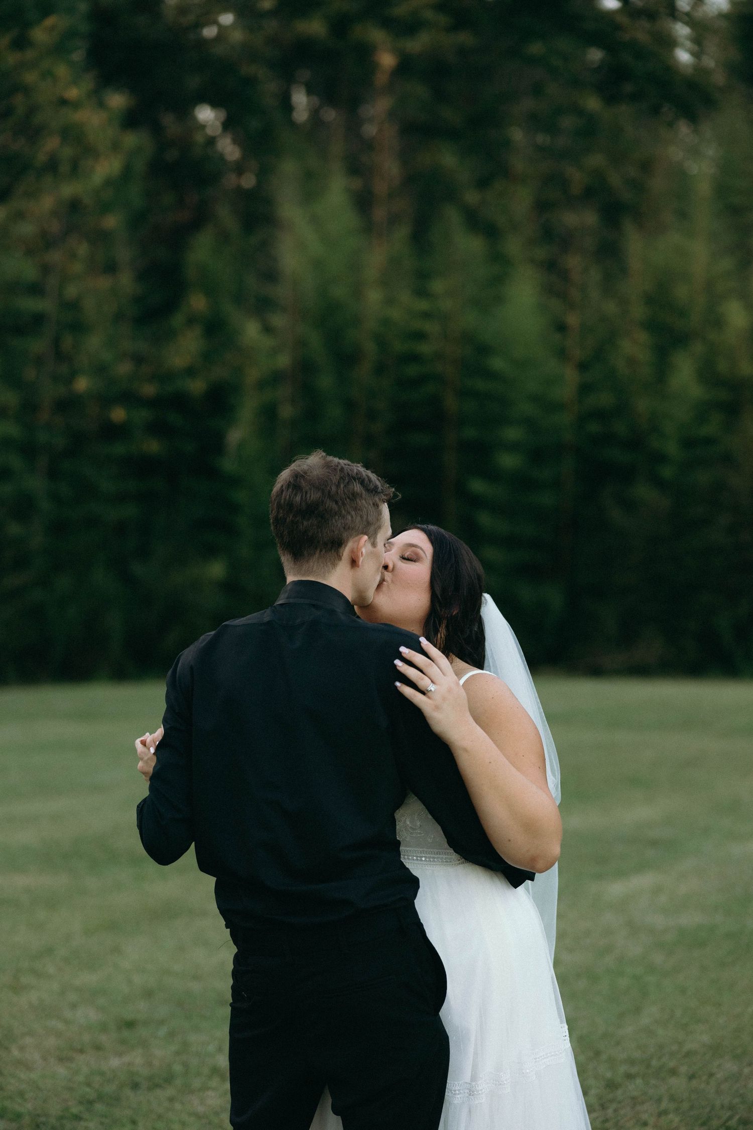 Romantic wedding photo of couple embracing outdoors with lush greenery in background.