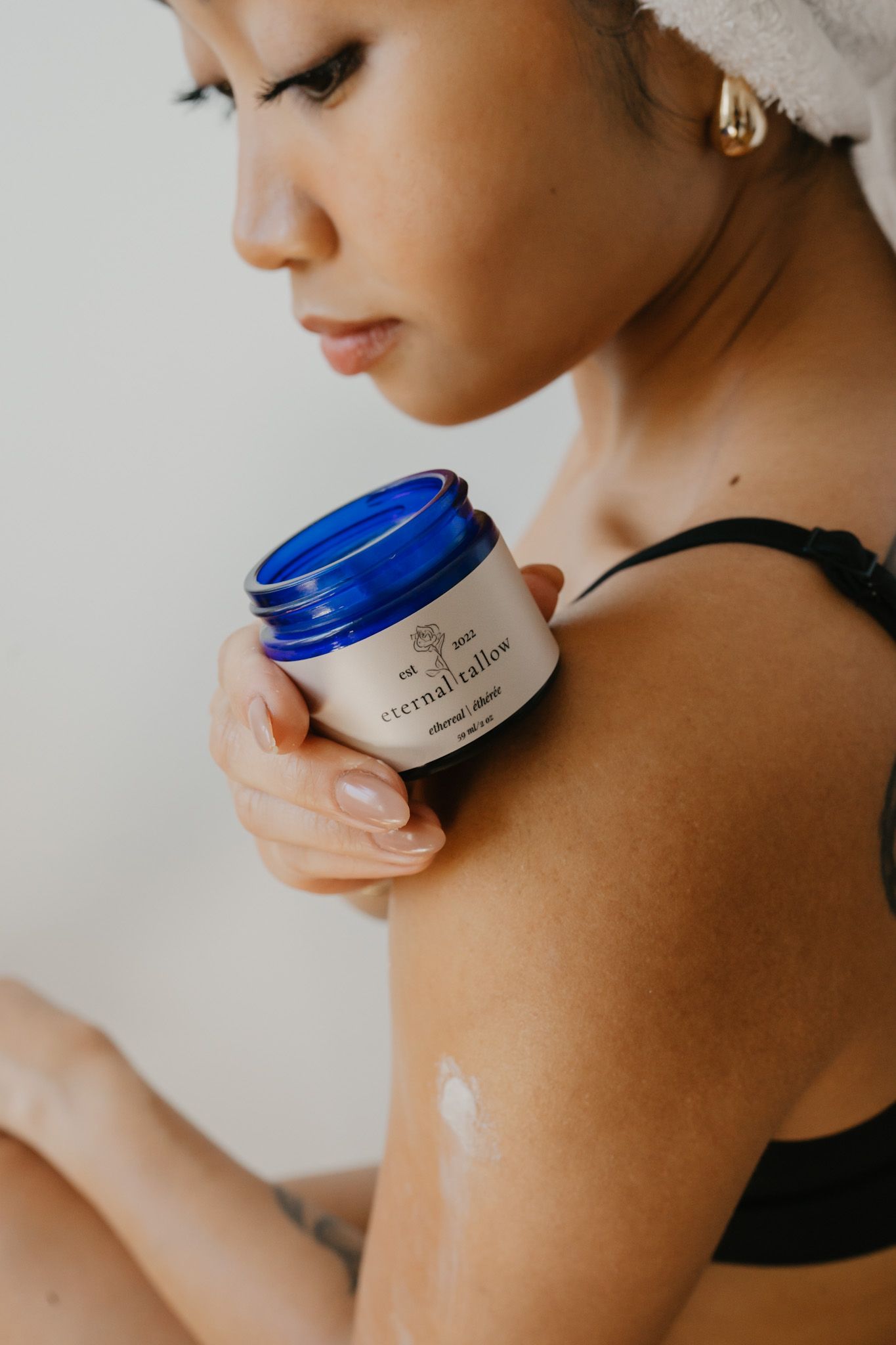 Person applying moisturizing cream from a blue jar onto bare shoulder in a skincare routine sequence.