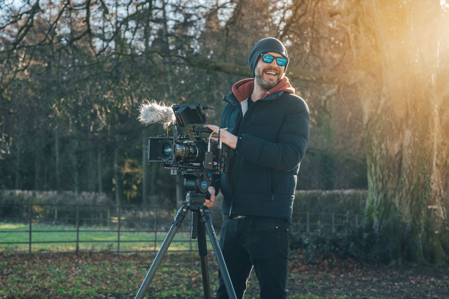 Camera equipment being set up outdoors during sunset with golden light filtering through trees.