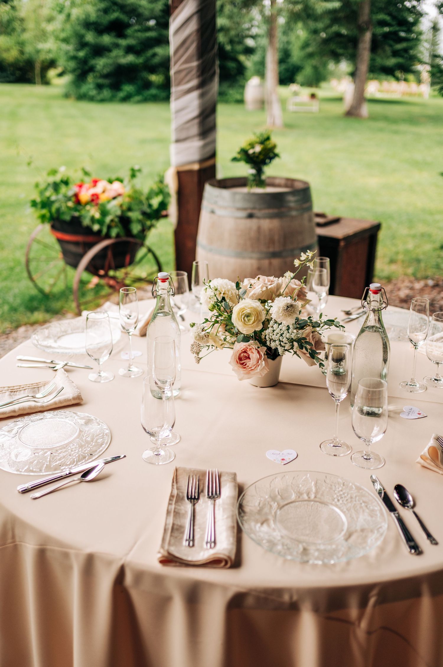 Elegant wedding reception table settings with white linens, floral centerpieces and crystal glassware in an outdoor venue.