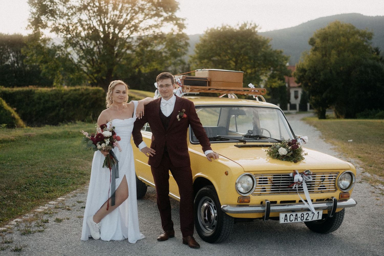 A classic yellow vintage car features prominently in an outdoor wedding photoshoot.