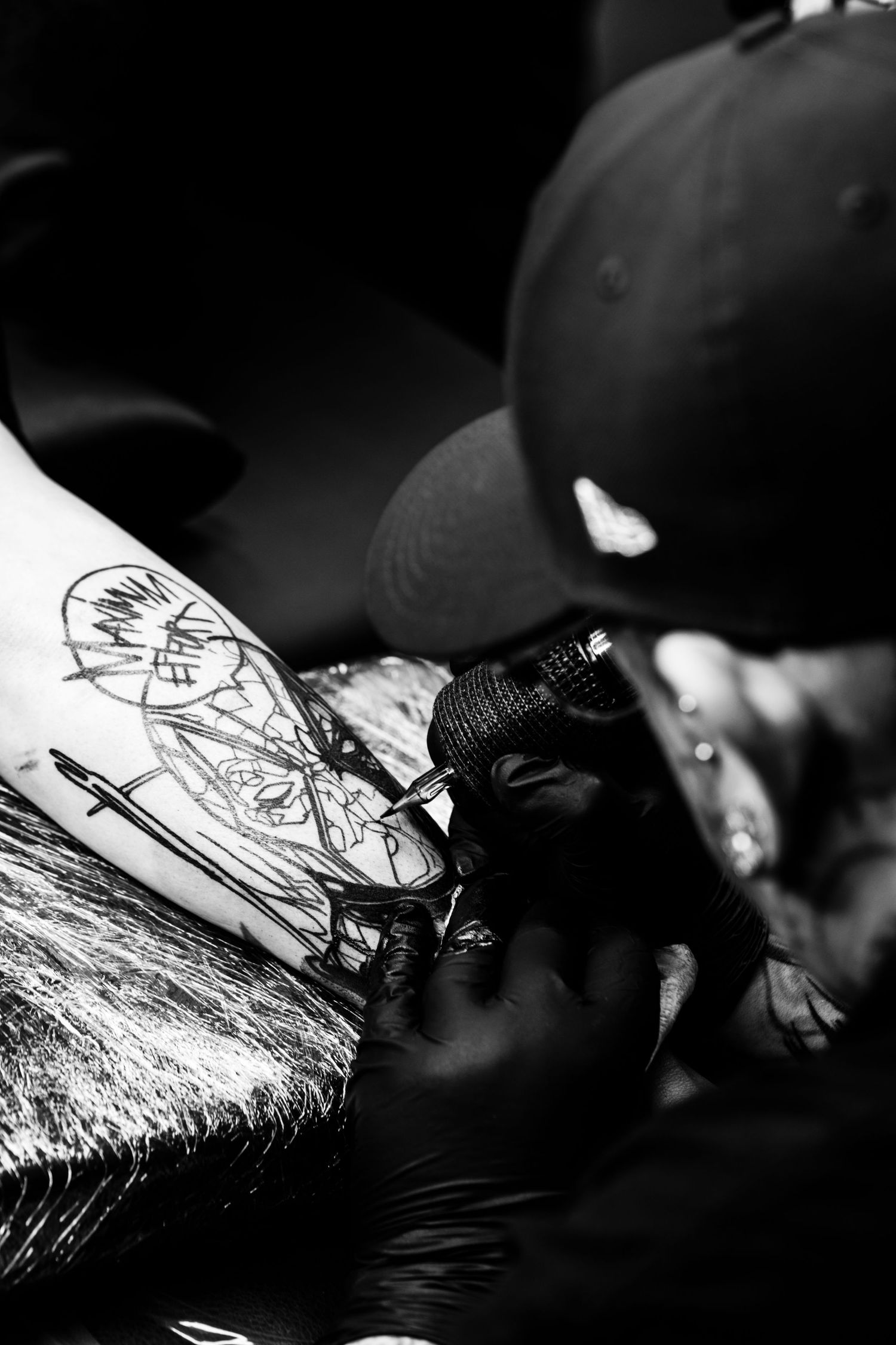 Close-up black and white shot of a tattoo artist at work wearing black gloves and creating a detailed design.