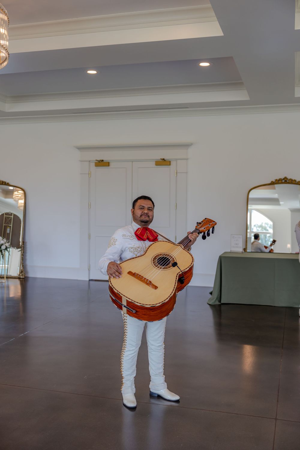 Musicians in white outfits perform with traditional guitars in an elegant reception hall.