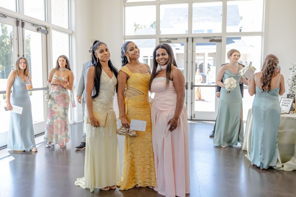 Group wearing pastel colored formal dresses stands in line against bright windows in an elegant venue.