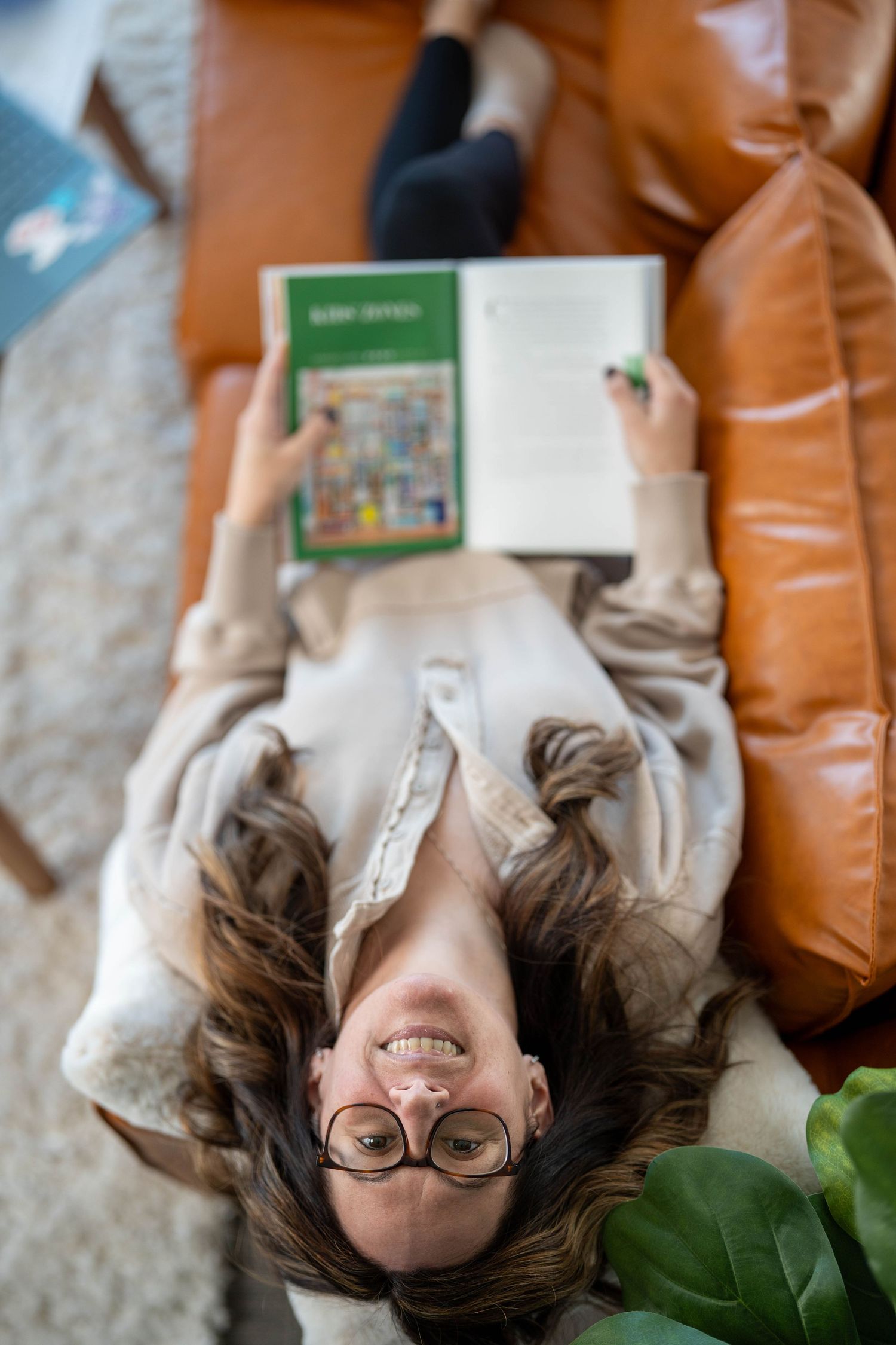 New Hampshire women in business having her branding photoshoot relaxing on brown leather couch in cream sweater with books.