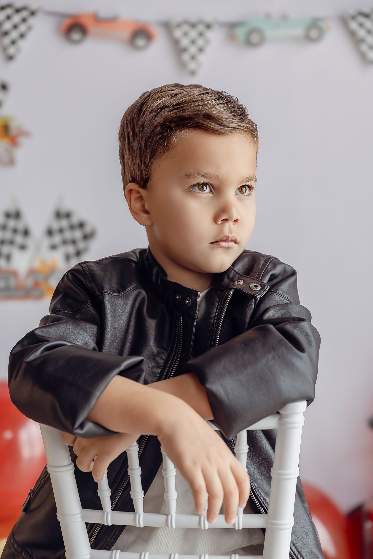 Detres Photography fotografiando a nino de 5 anos sentado en una silla mirando hacia el lado tiene una chaqueta negra de cuero