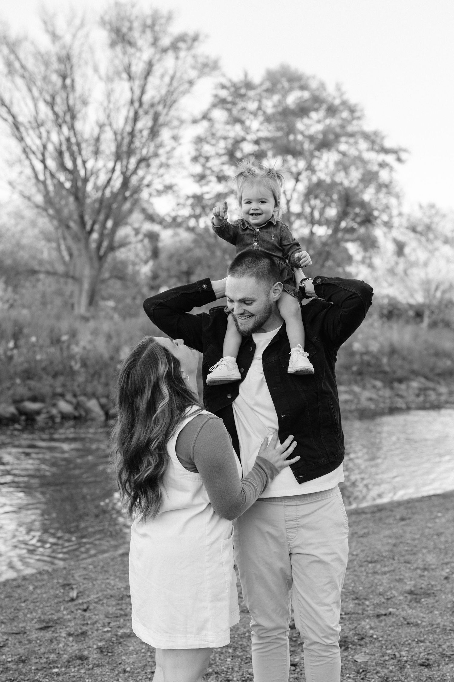 A couple shares romantic moments by a lake in black and white photos showing playful interaction and affection.
