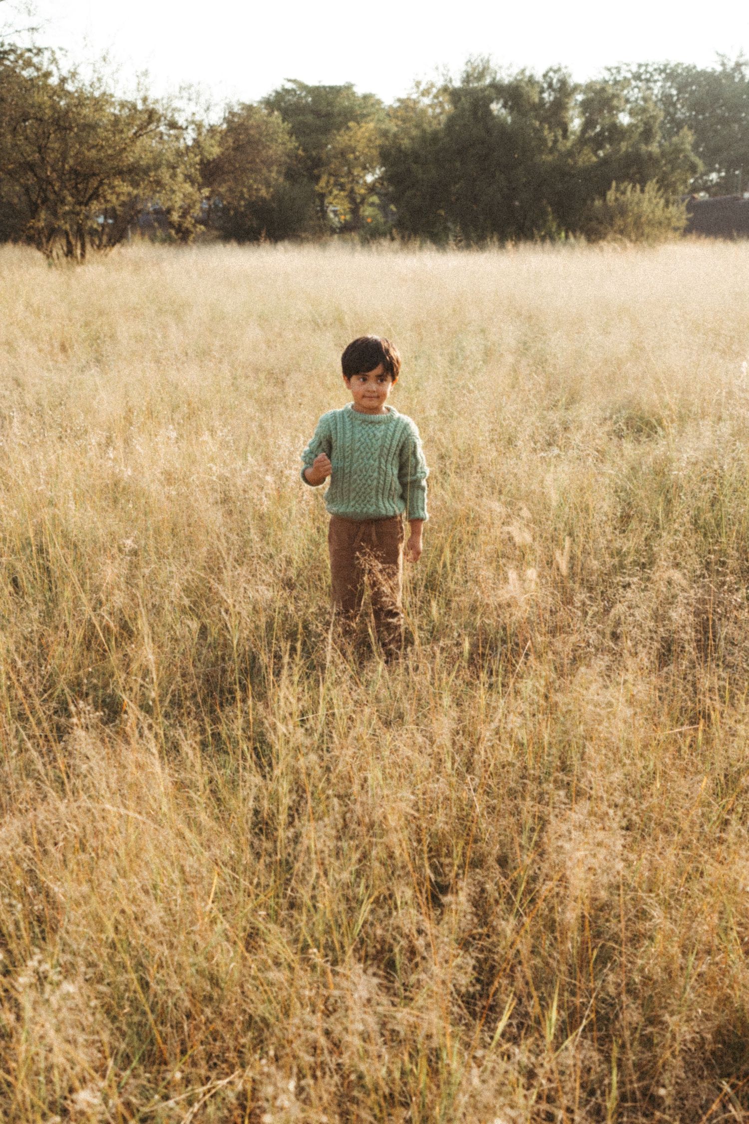Child in mint green sweater standing alone in a field of golden grass.