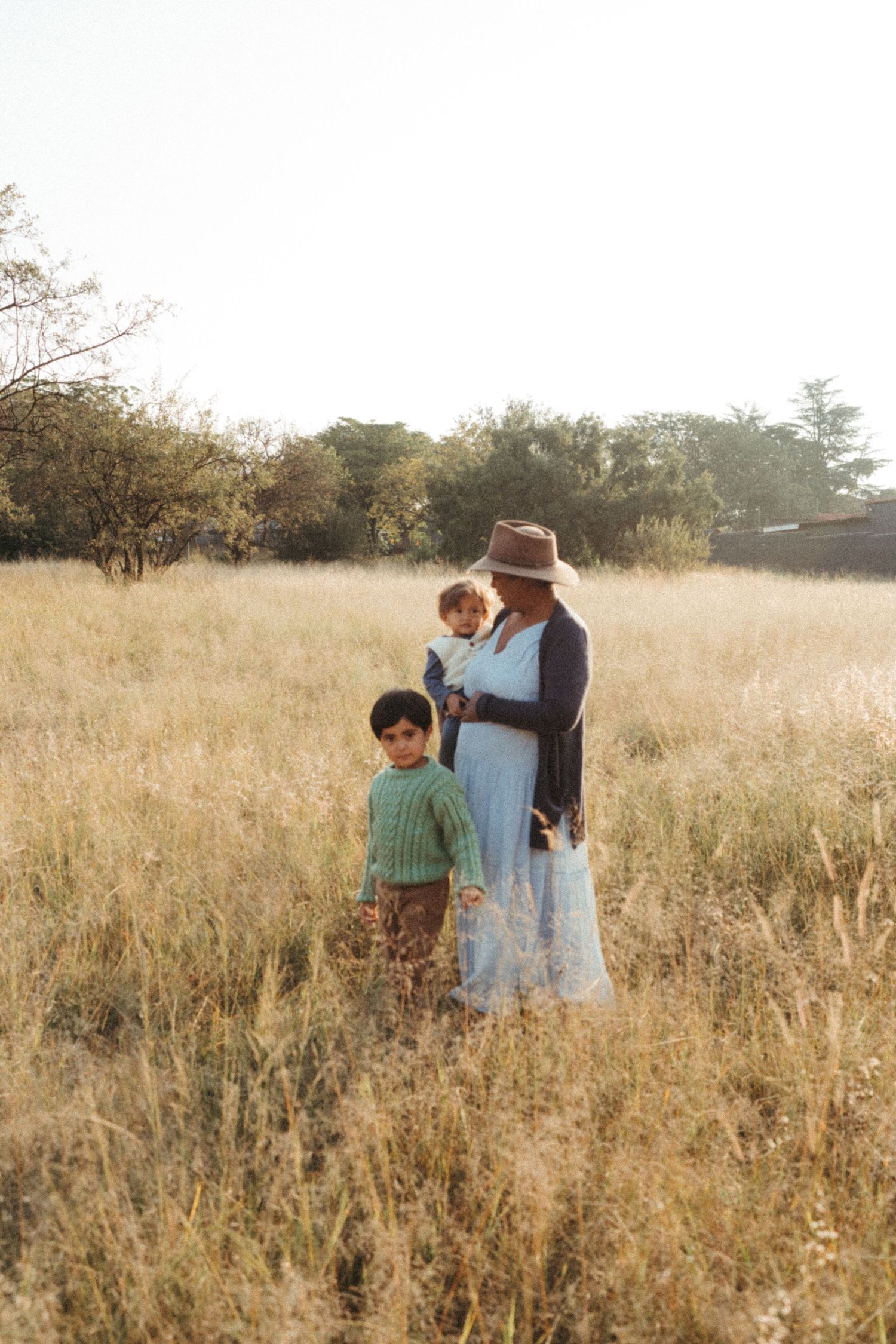 Family members walk together through a sunlit meadow of dried grass.