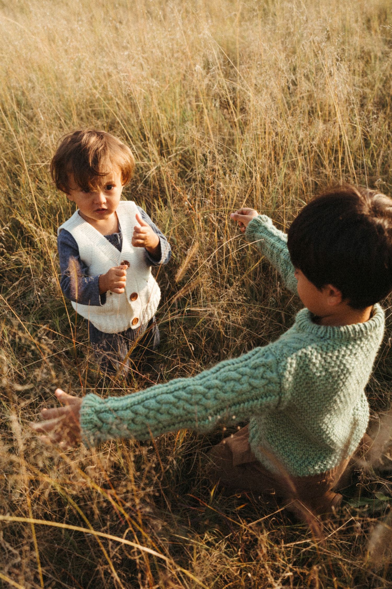 Children play and tumble in tall dried grass during sunset.