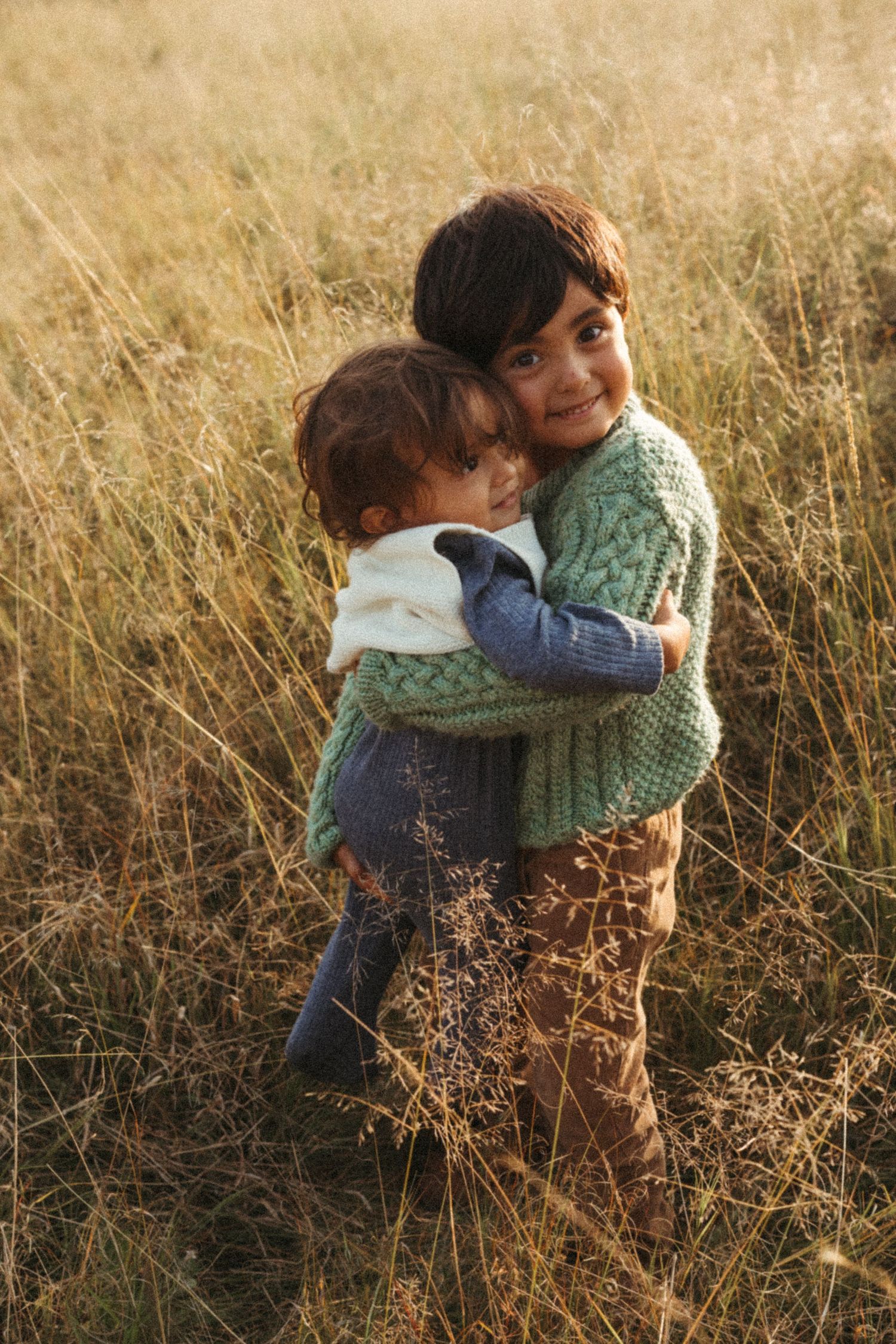Two children embrace while playing in a golden field at sunset.