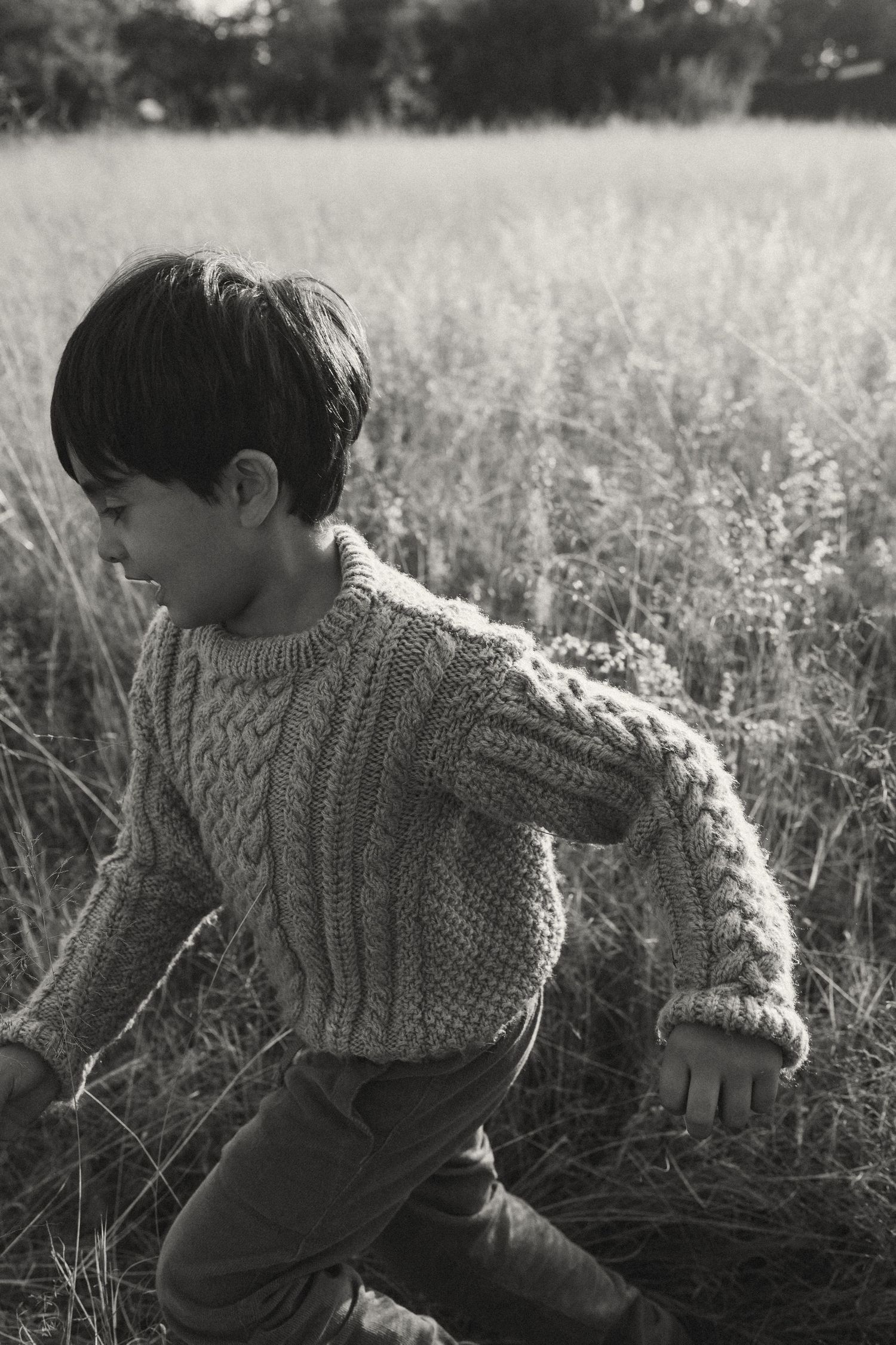 Child wearing cable knit sweater runs through a misty field in black and white.