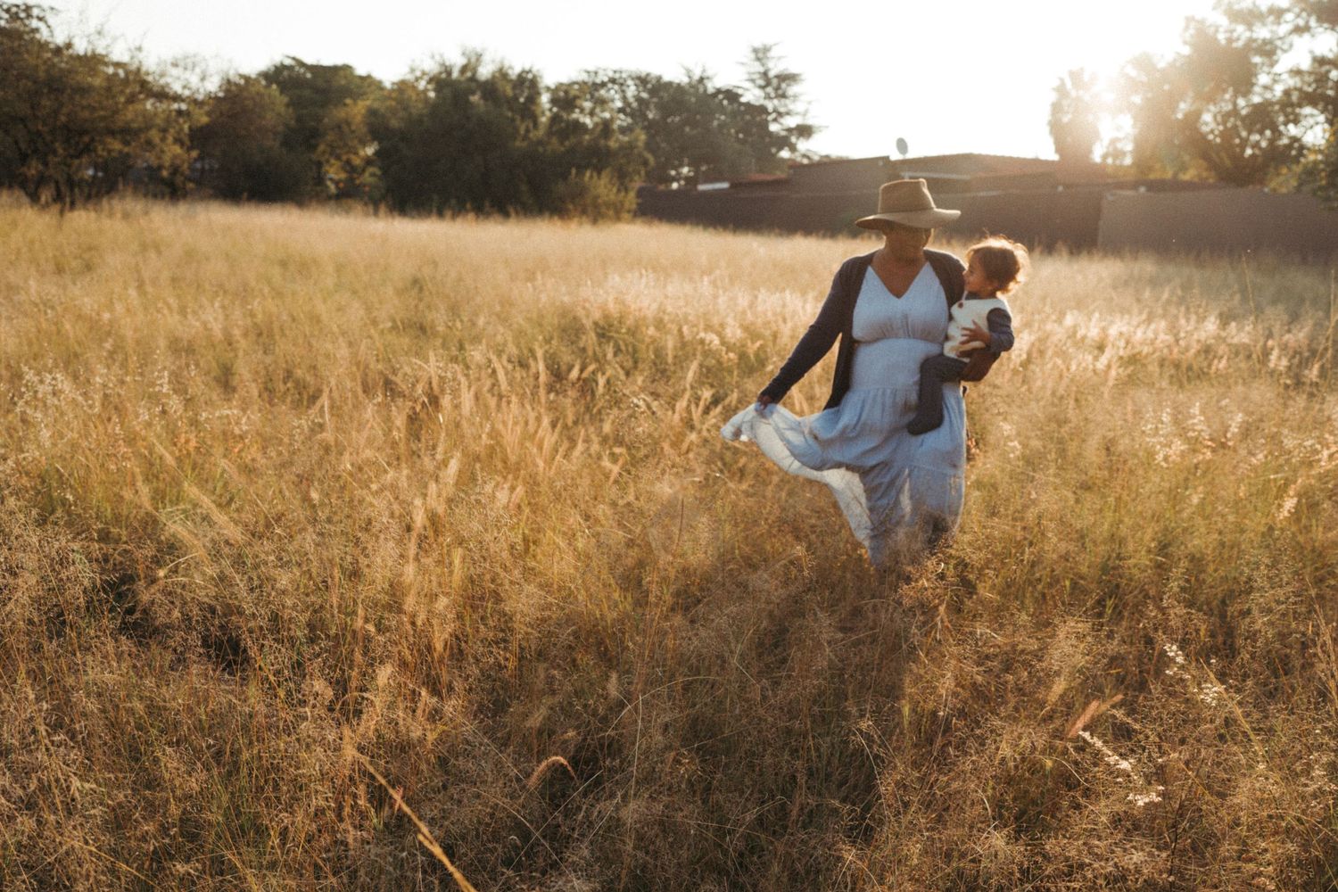 Couple walking through tall grass field at sunset.