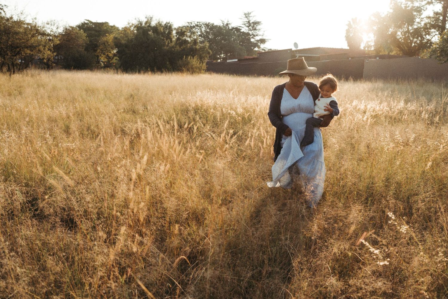 Family enjoying a walk through golden grass field at sunset.