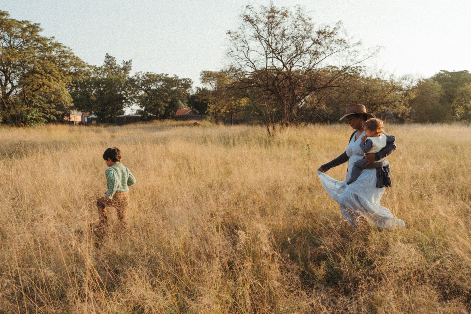 People playing and dancing together in a sunlit meadow of tall grass.