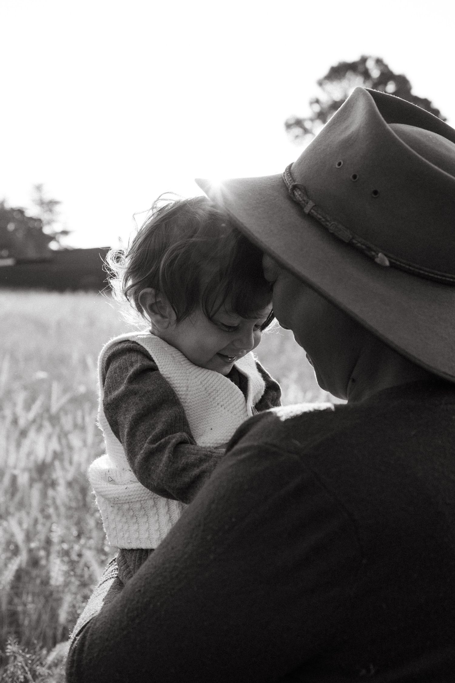 Black and white intimate portrait of two people against a field backdrop.