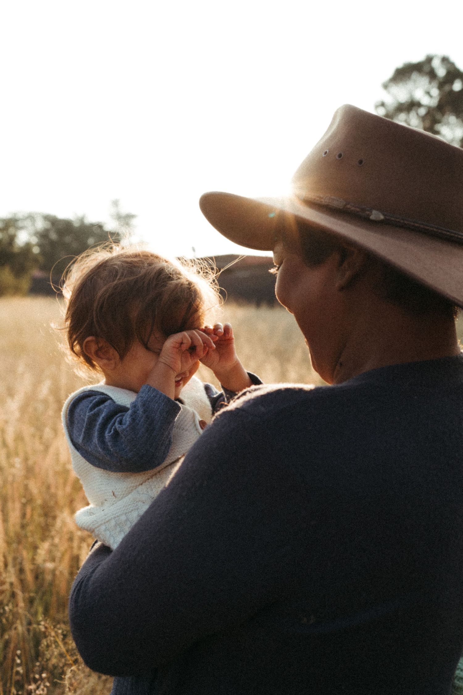 Side profile of two people embracing in golden sunlight with grass in background.