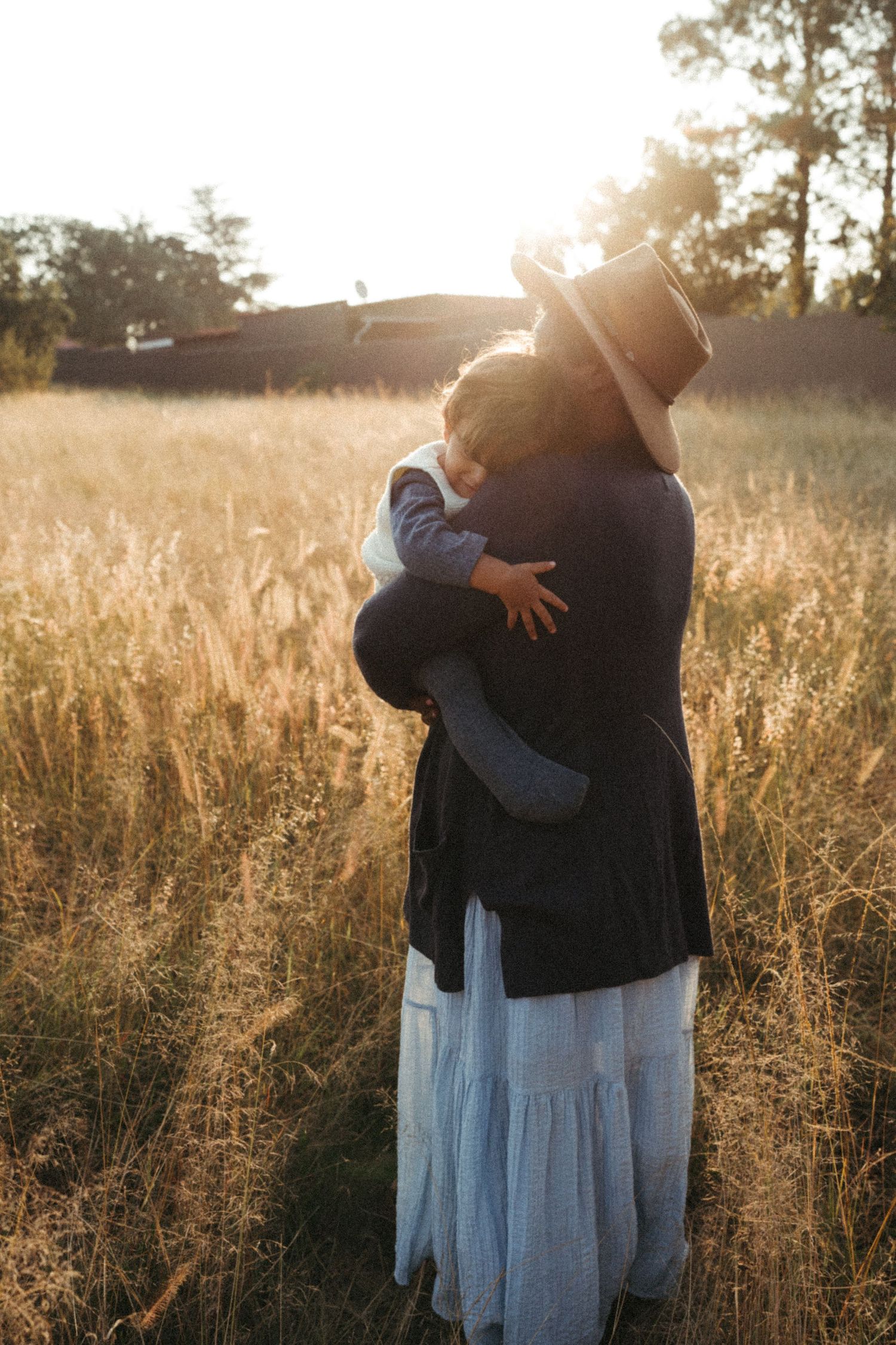 Two figures embrace in a sunlit field with golden grass and trees in background.