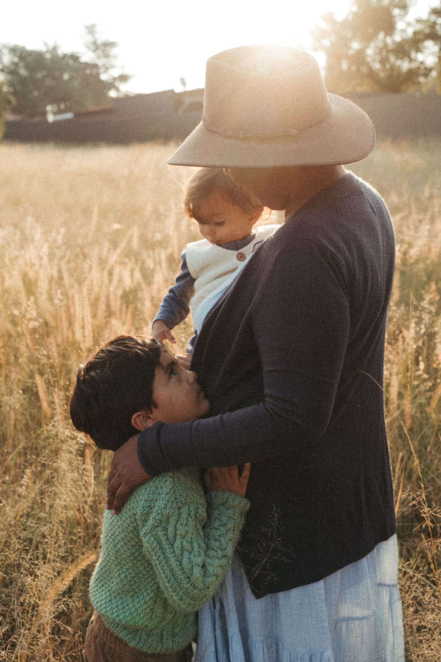 A tender moment captured in a sunlit field with tall grass and a warm sunset glow.