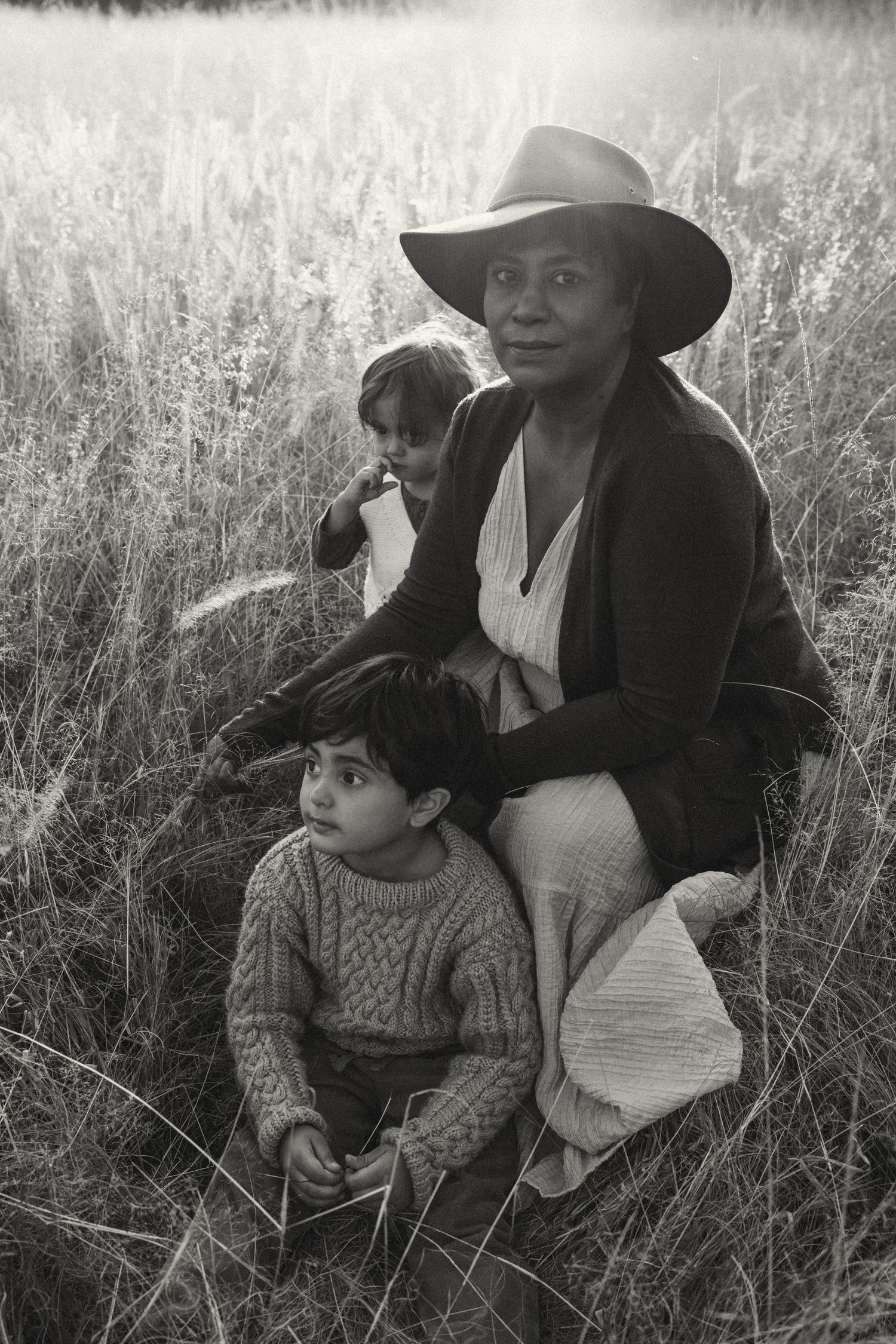 Black and white image of two figures sitting together in a wild grass meadow.