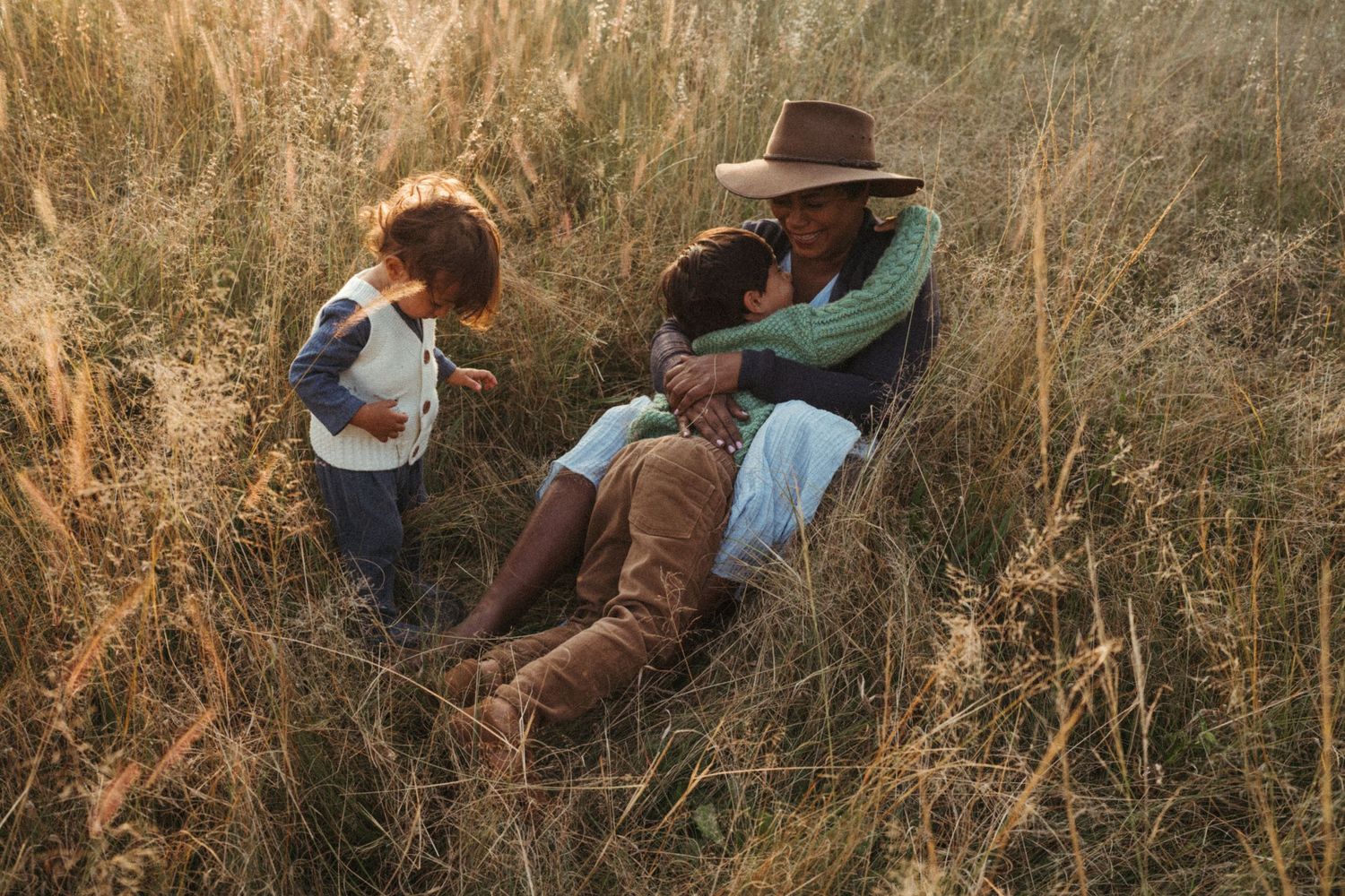 Warm-toned photograph of two people sharing quiet moments in tall grass.