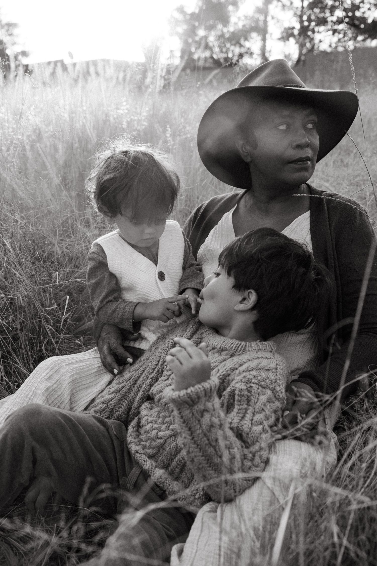 A tender black and white portrait of parent and child sharing an intimate moment in tall grass at sunset.