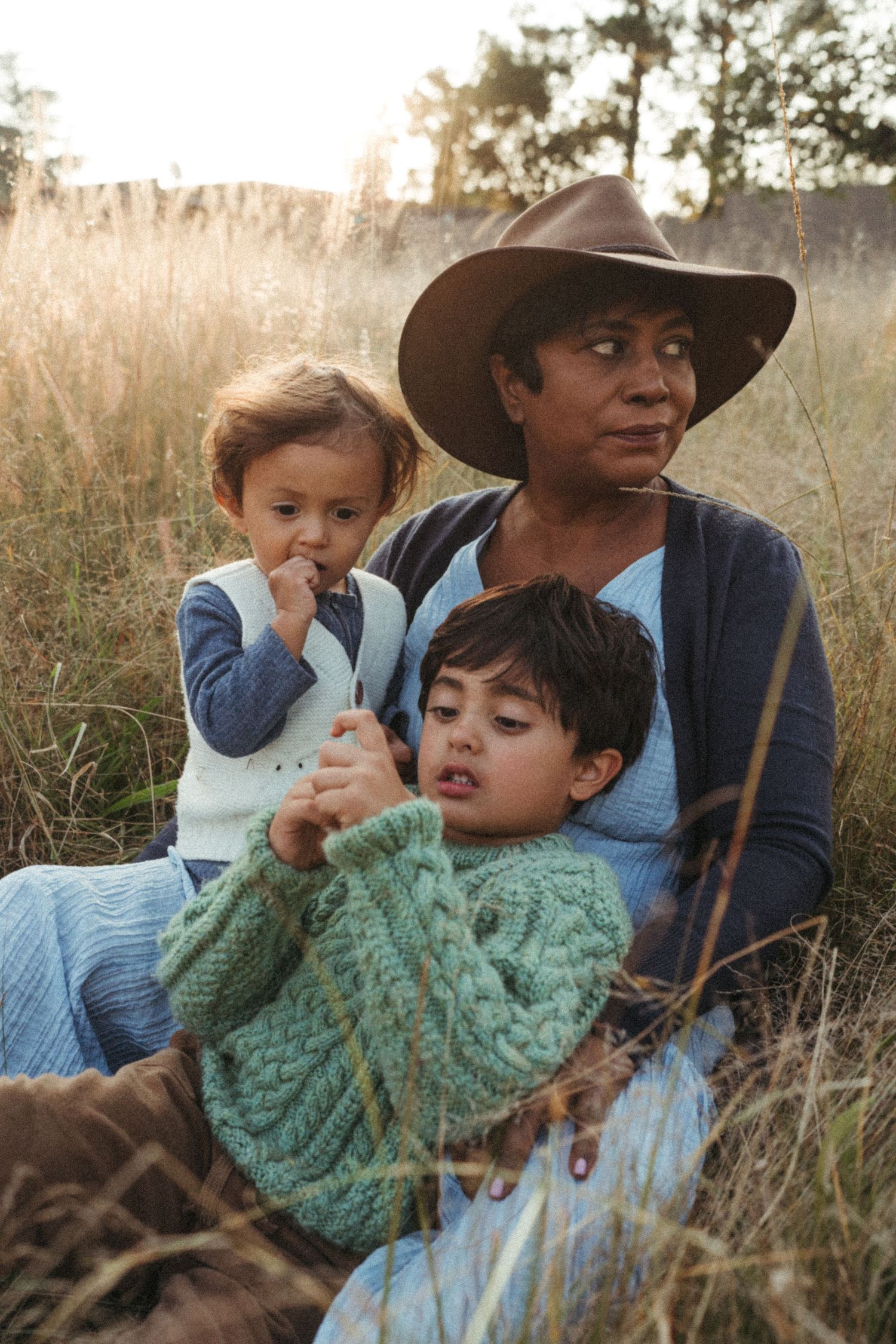 Family wearing casual clothes sits together in golden field during sunset.
