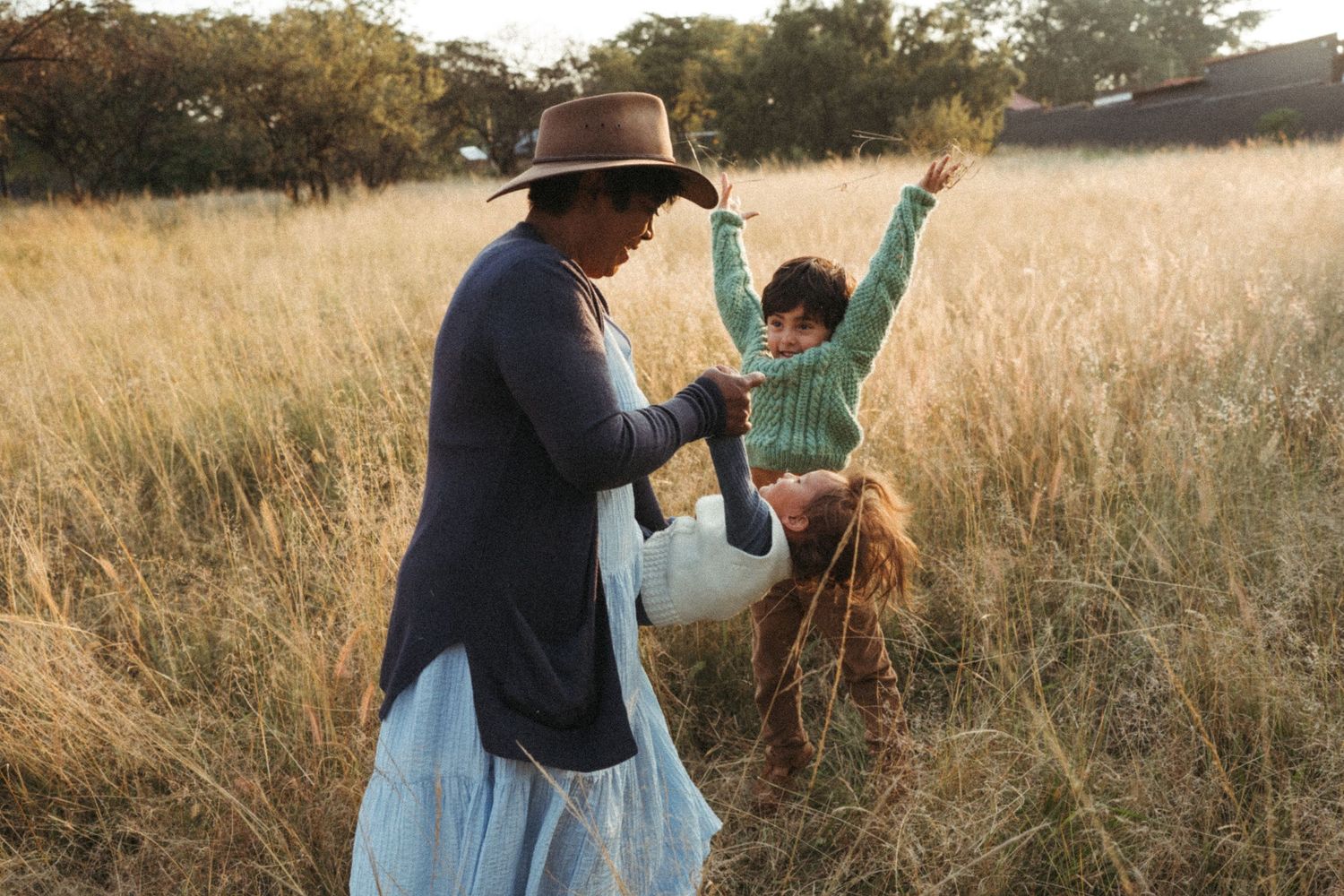 Family spending time together in golden field during sunset wearing casual attire.