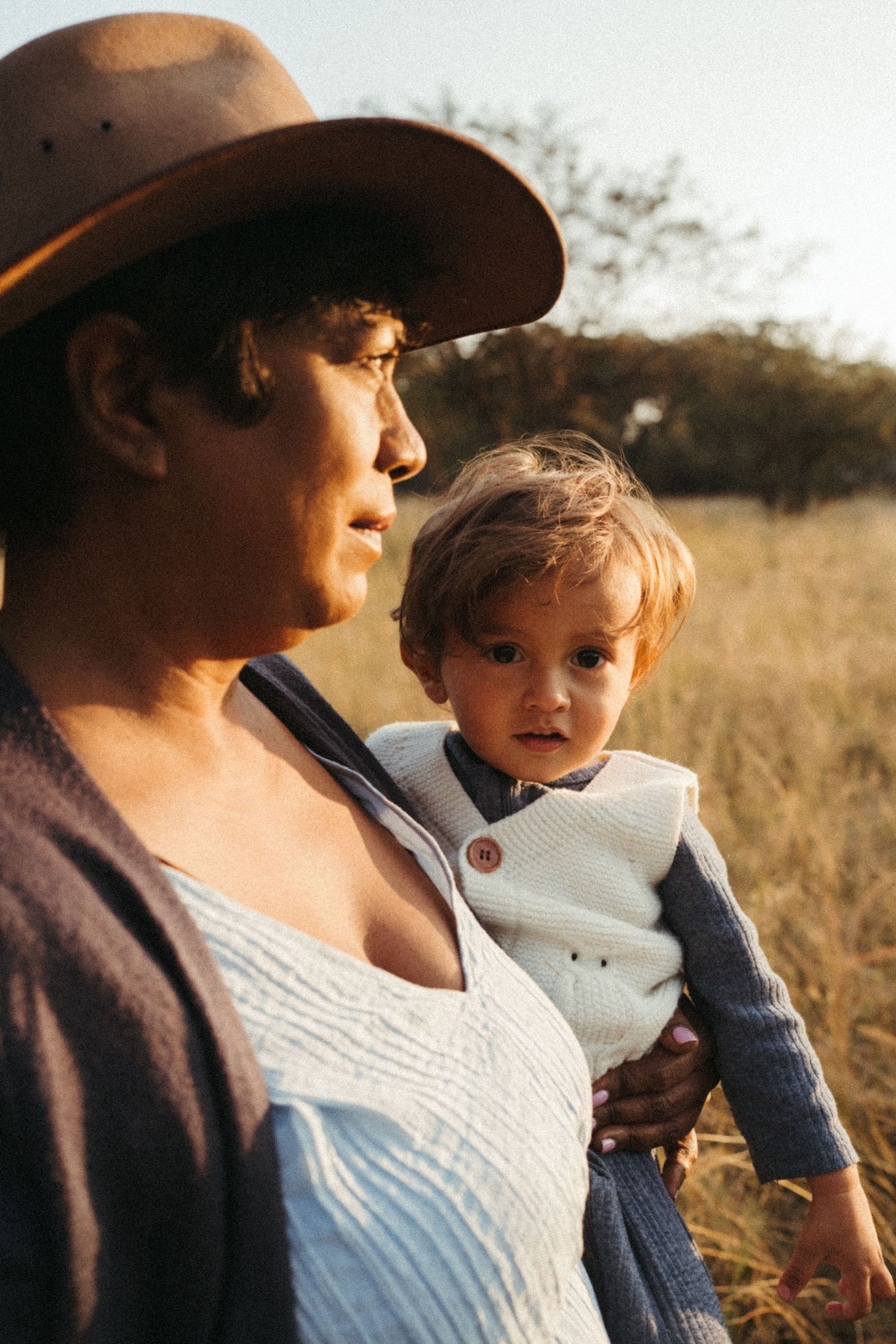 Intimate family portrait captured during sunset in field with brown hat and white dress.