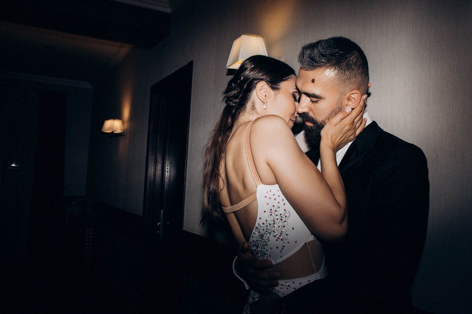 A romantic couple shares an intimate moment in formal attire during what appears to be their wedding celebration.