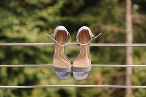 A row of elegant silver and lavender bridesmaid shoes lined up outdoors against a natural green background.