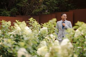 A couple poses together in a lush garden setting with white hydrangea flowers in the foreground.