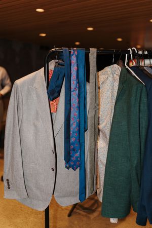 Clothing rack displaying casual menswear with grey shirts, blue ties, and green jackets hanging neatly in a store.