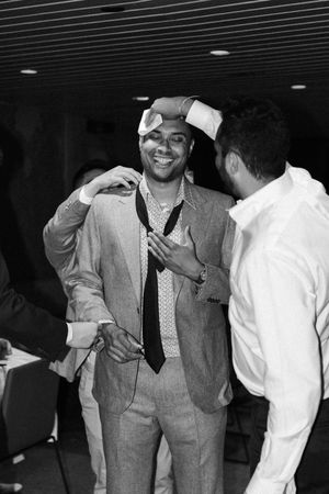 Two people share a lighthearted moment in black and white, with one wearing a suit and tie during what appears to be a casual chat.