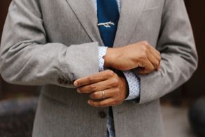 Close-up view of hands adjusting a gray suit jacket sleeve and cuff link.