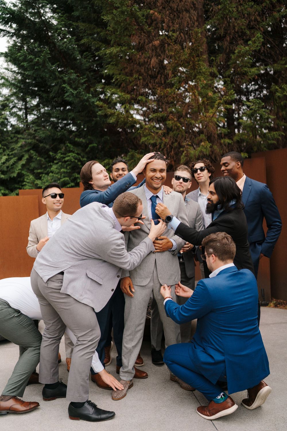 Wedding party members in gray suits and one in blue pose playfully for a series of candid group photos outdoors.