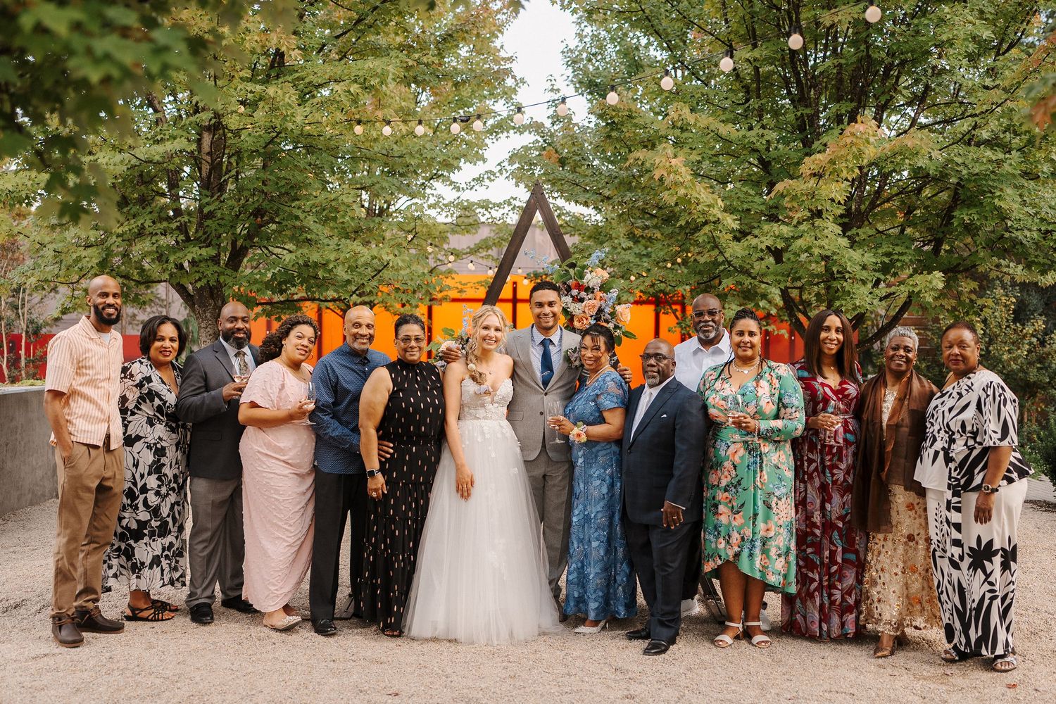 Wedding party and guests pose together in a series of outdoor group photos under green trees.