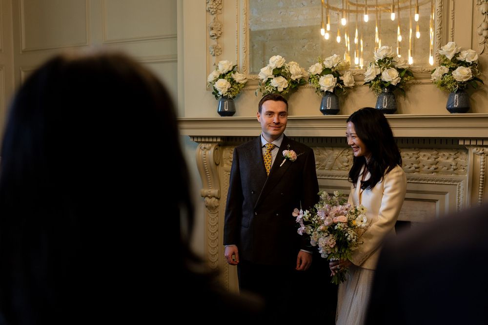 A couple embraces on their wedding day in a dimly lit venue decorated with string lights and floral arrangements.