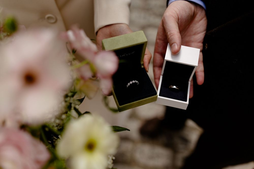 Close-up view of hands exchanging rings during a wedding ceremony with pink cherry blossoms in the background.