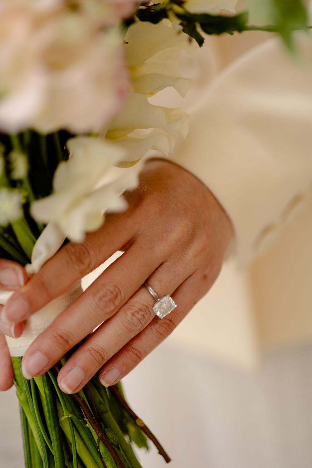Close-up view of hands holding white flowers with a sparkling diamond engagement ring prominently displayed.