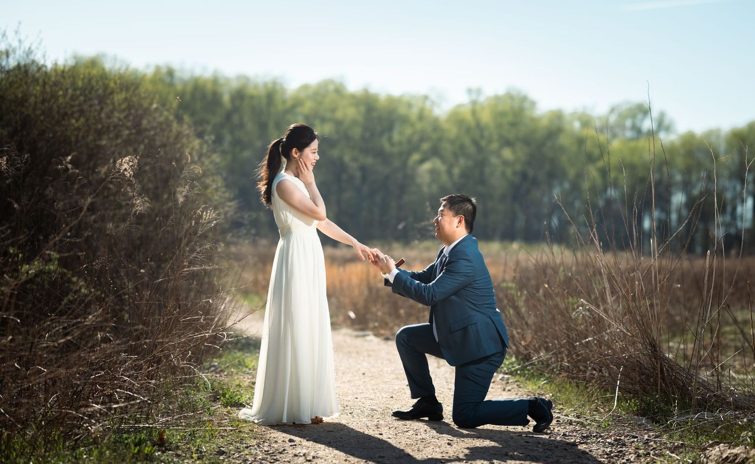 Newlyweds share intimate moments along train tracks on a sunny spring day with natural landscape in background.