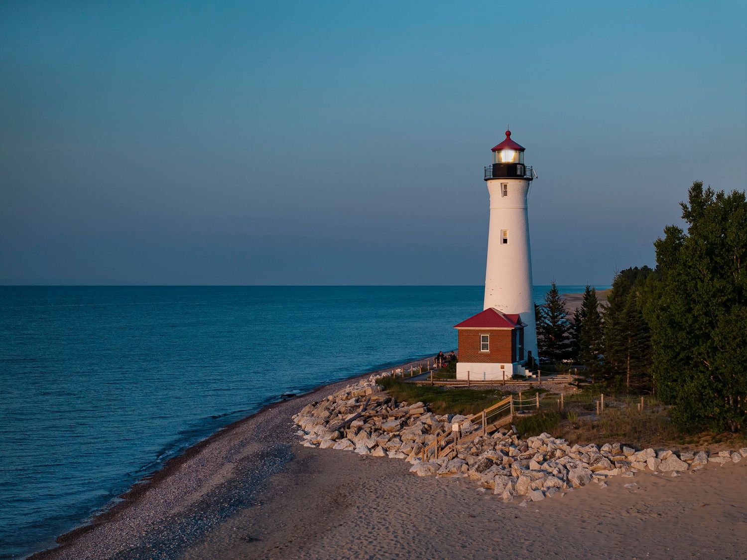 A white lighthouse tower stands on a rocky shoreline against turquoise waters of Lake Huron at Crisp Point, Michigan.