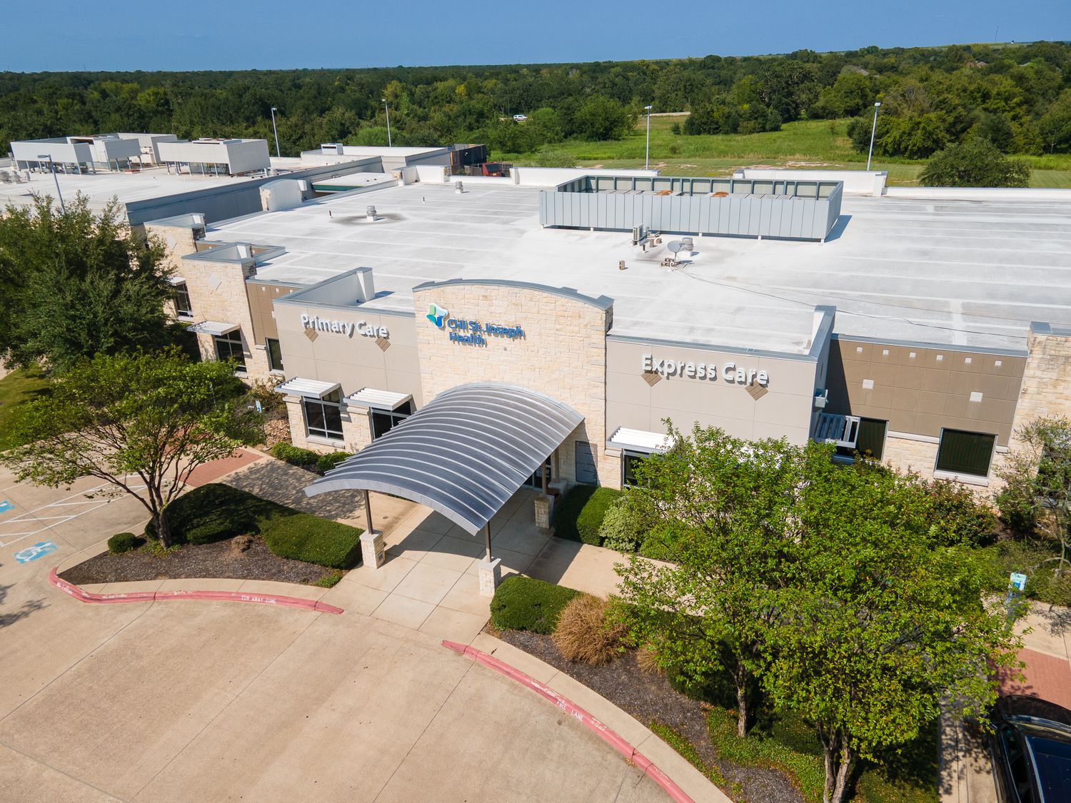 Aerial view of a commercial building complex with white roofs and parking lots surrounded by green landscape.