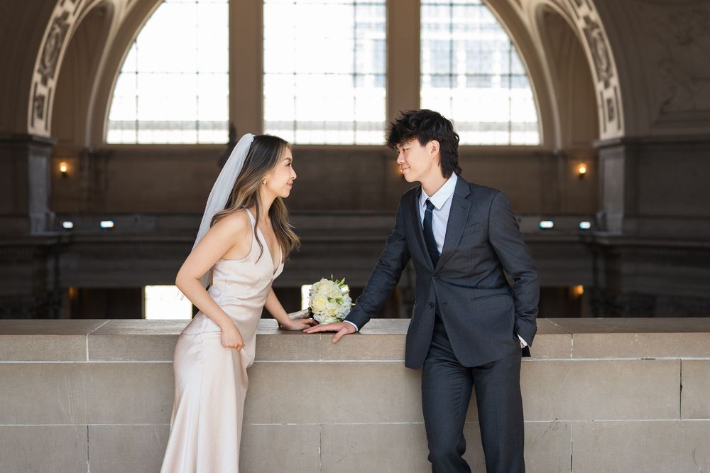 Elegant couple shares romantic moments in a rustic industrial venue with large windows and exposed brick walls.