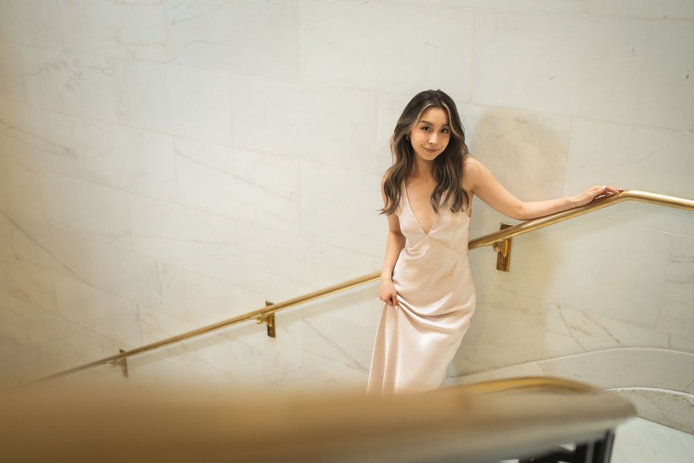 Bride in blush dress poses along a staircase railing in an elegant indoor setting.