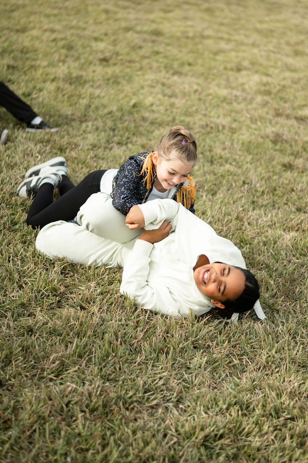Two people playfully wrestling and laughing together on grass outdoors.