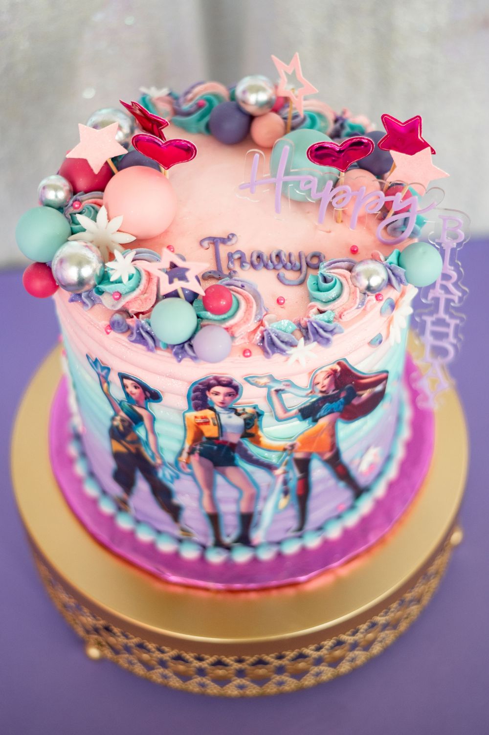 Pink and turquoise decorated cake with heart-shaped fondant decorations sits on a gold platter.