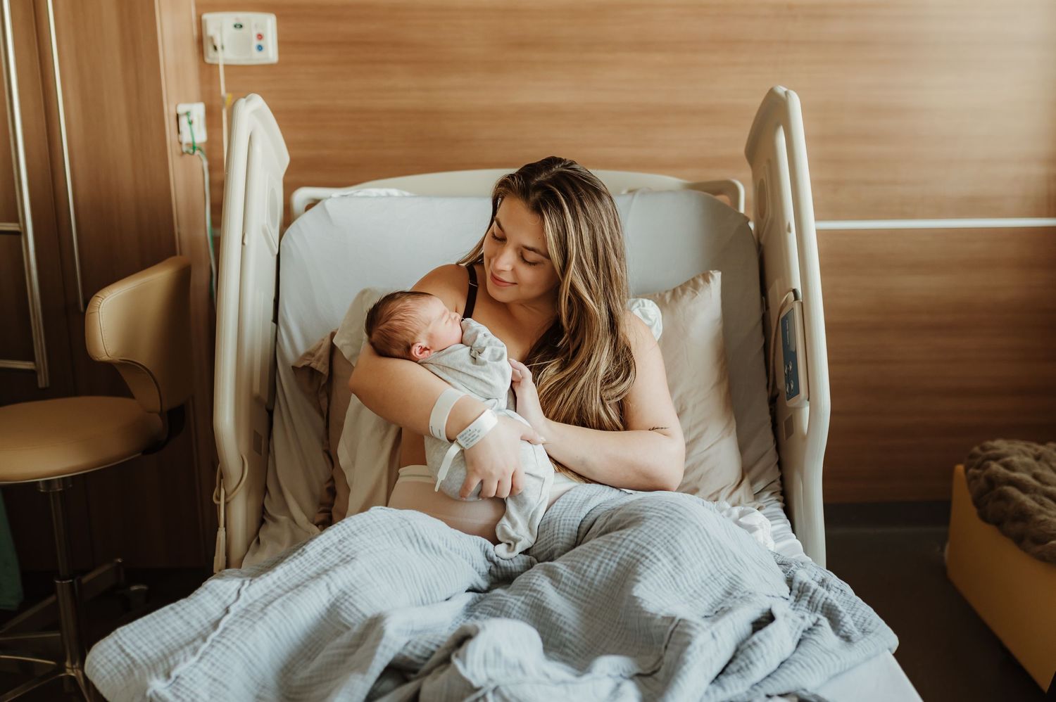 A tender moment between parent and newborn baby lying together on a hospital bed.