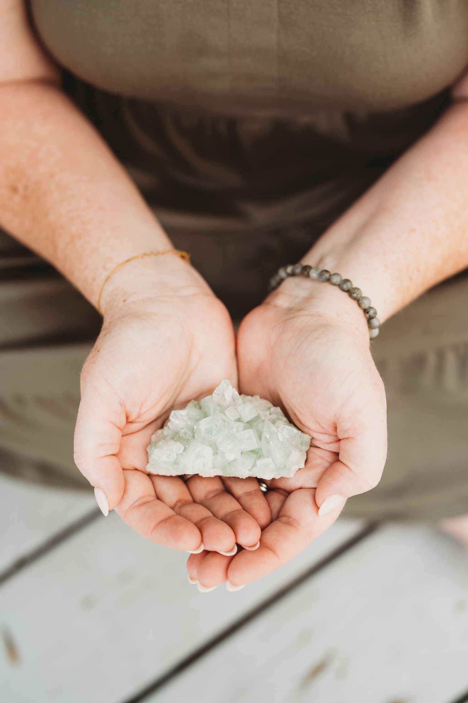 Hands cupping and displaying white rock salt or bath salts against a light gray background.