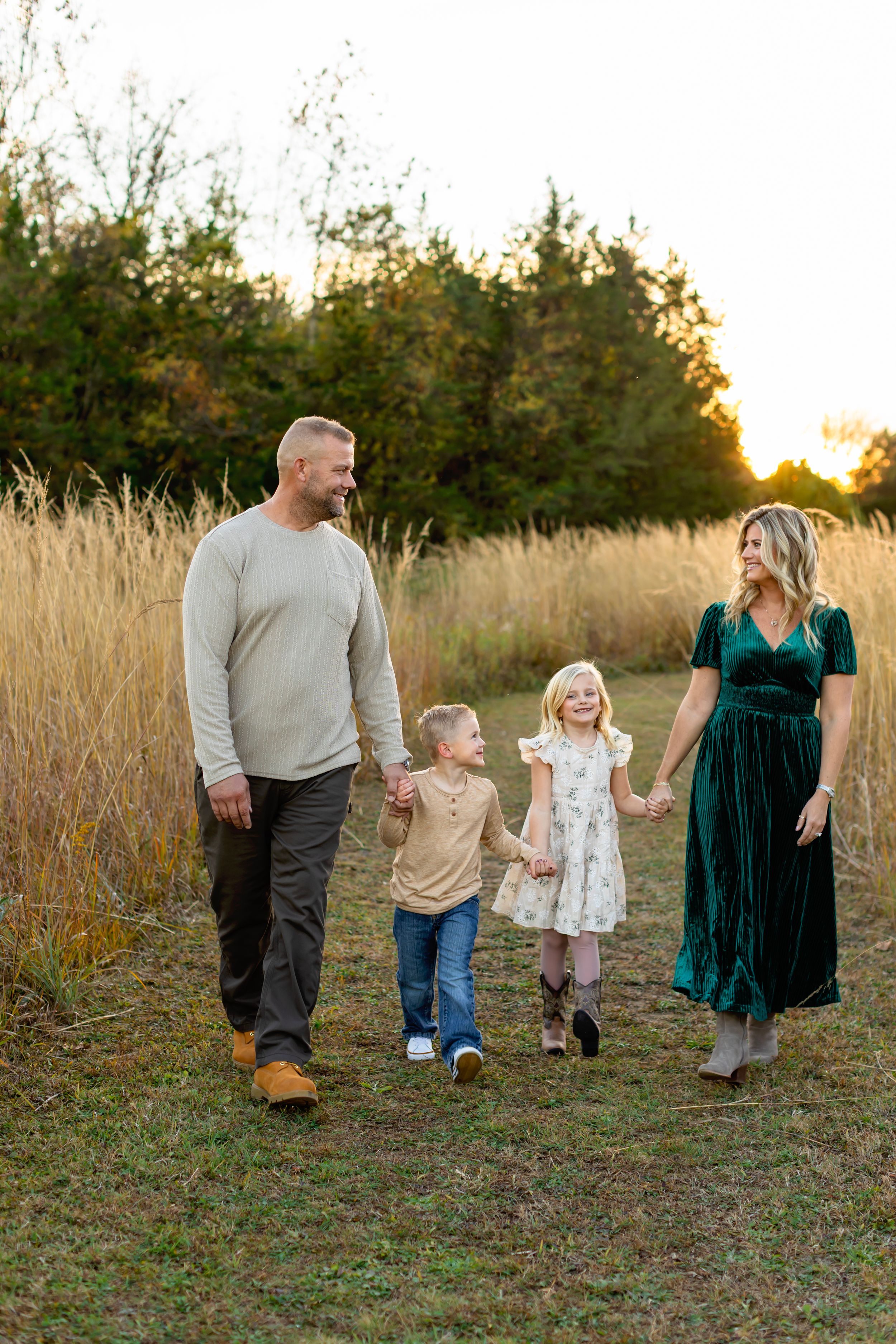 A family walks together through a golden field at sunset while holding hands.